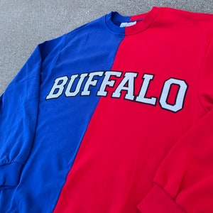 May include: A red and blue long-sleeved sweatshirt with the word "BUFFALO" in white letters with black outlines.