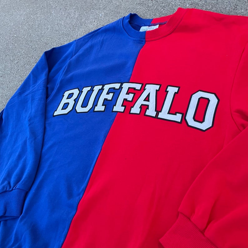 May include: A red and blue long-sleeved sweatshirt with the word "BUFFALO" in white letters with black outlines.