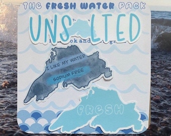 May include: A set of two blue and white stickers featuring the outline of a lake with the text "THE FRESH WATER PACK UNSALTED" and "I LIKE MY WATER SODIUM FREE" on one sticker and "FRESH" on the other.