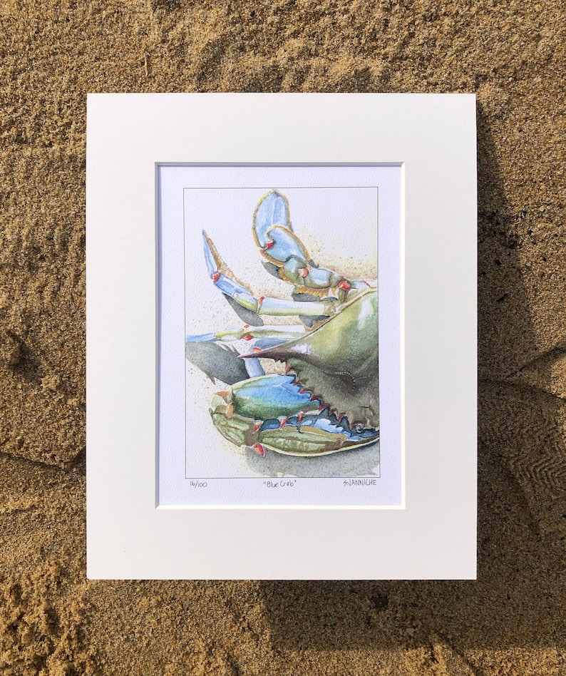 May include: A framed watercolor print of a blue crab, set against a sandy background. The crab is depicted in shades of blue, green, and tan, with intricate details. The print is titled "Blue Crab" and is numbered 16/100.