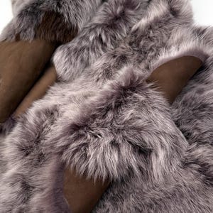 May include: A close-up shot of a luxurious, grey fur textile with a soft, plush texture. The fur is a mix of light and dark grey tones, with patches of brown suede-like material visible. The overall effect is one of warmth and opulence.