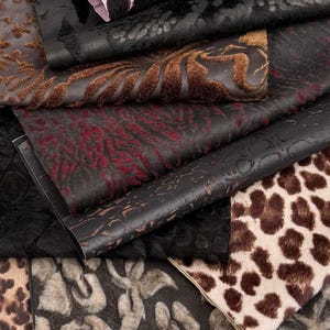 May include: A collection of stacked fabric swatches featuring various textures and patterns, including animal prints like leopard and tiger, floral motifs, and geometric designs in shades of black, brown, tan, and deep red with a soft, fuzzy finish.