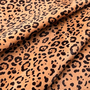 May include: A close-up of a brown and black leopard print fabric. The fabric has a soft, fuzzy texture.
