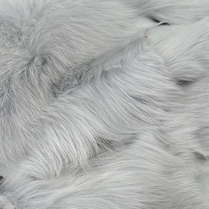 May include: Close-up of a soft, fluffy, light grey faux fur fabric. The fur is arranged in a wavy pattern, creating a luxurious and cosy texture.