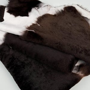 May include: A brown and white cowhide rug with a soft, plush texture. The rug is folded in half, revealing the white underside.