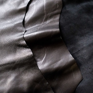 May include: Two pieces of black leather, one smooth and one textured, are folded together. The leather is soft and supple.