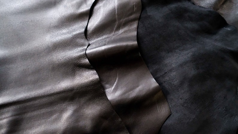 May include: Two pieces of black leather, one smooth and one textured, are folded together. The leather is soft and supple.