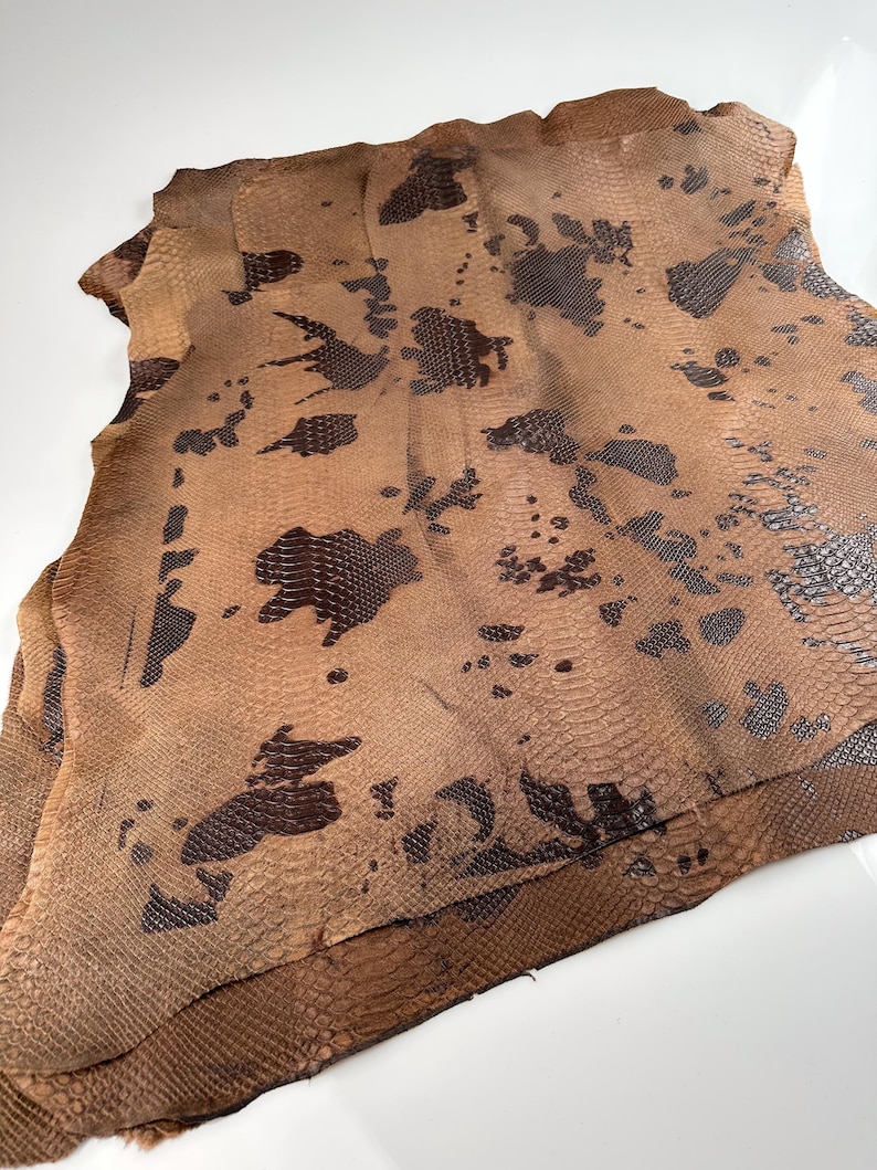 May include: A piece of brown snakeskin leather with a dark brown pattern. The leather is folded in half and has a rough texture.