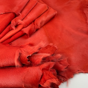 May include: A stack of red cowhide leather hides with a fuzzy texture. The hides are folded and arranged in a pile.