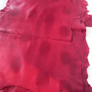 Pu&ograve; includere: Una pila di pelli di cuoio rosso scuro con una superficie liscia e leggermente strutturata. Il cuoio &egrave; piegato e ha una forma leggermente irregolare.