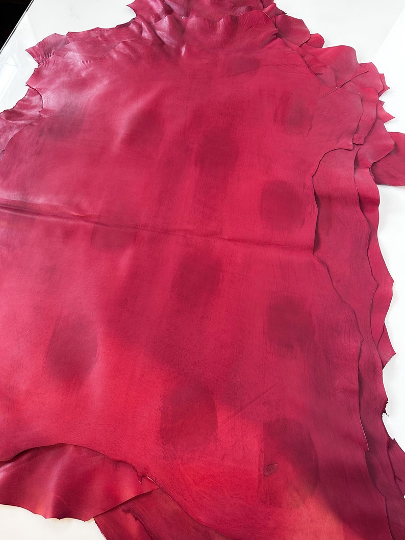 Pu&ograve; includere: Una pila di pelli di cuoio rosso scuro con una superficie liscia e leggermente strutturata. Il cuoio &egrave; piegato e ha una forma leggermente irregolare.