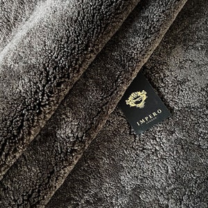 May include: Close-up of a dark grey faux fur fabric with a black tag that reads "Impero London".