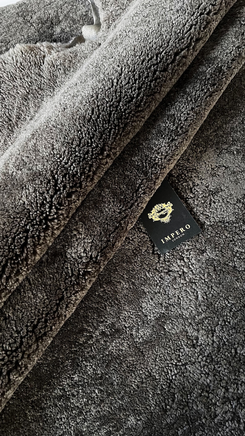May include: Close-up of a dark grey faux fur fabric with a black tag that reads "Impero London".