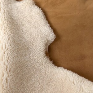 May include: A white sheepskin rug with a brown suede backing. The rug is soft and fluffy, and the suede is smooth and supple.
