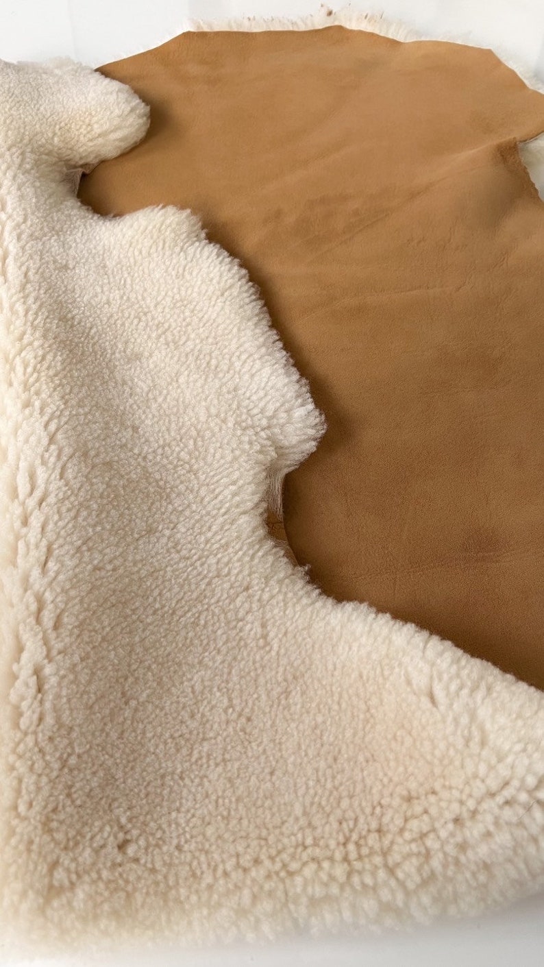 May include: A white sheepskin rug with a brown suede backing. The rug is soft and fluffy, and the suede is smooth and supple.