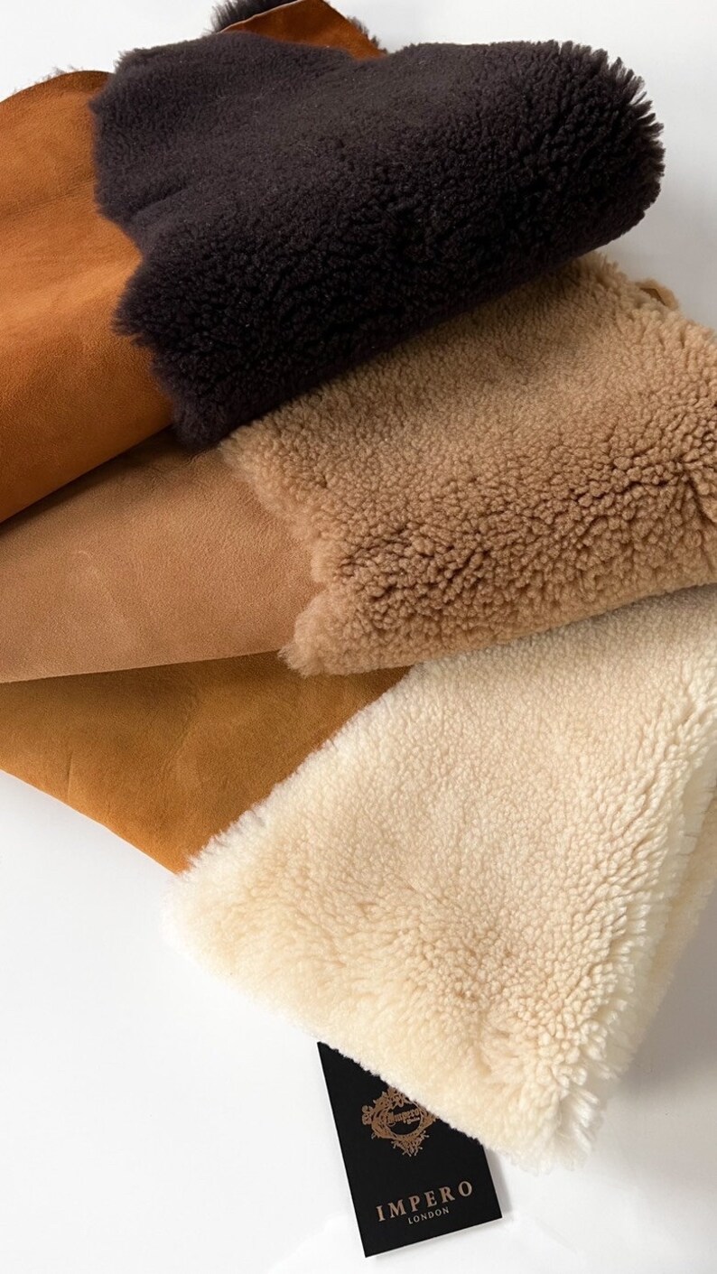 May include: Four pieces of sheepskin in different colors: brown, tan, light brown, and white. The sheepskin is soft and fluffy. The sheepskin is arranged in a stack, with the brown sheepskin on top. The sheepskin is labeled with the brand name "Impero London".