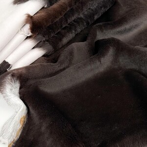 May include: A close-up of a brown faux fur fabric. The fabric is soft and fluffy, with a long pile. It is folded in several layers, showing the texture of the fur.