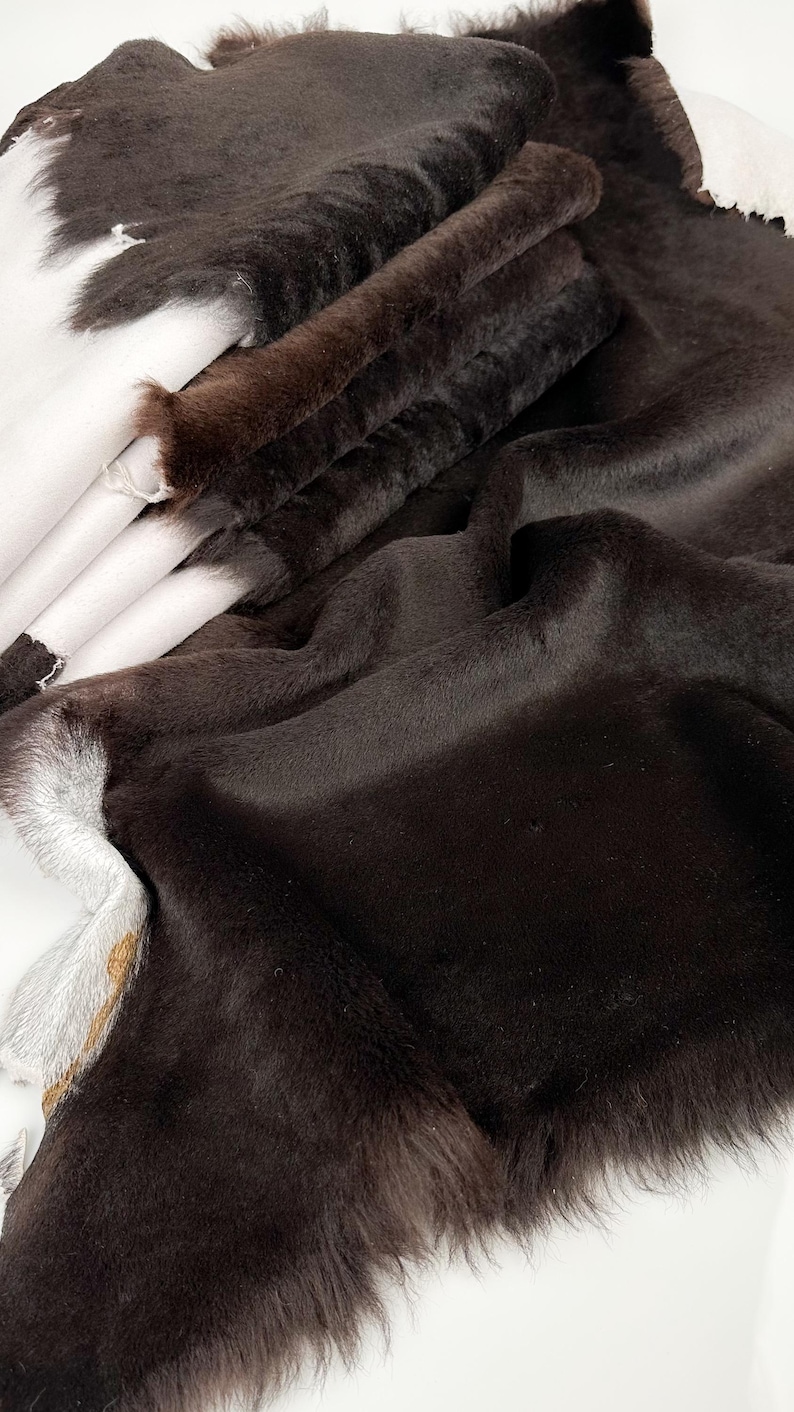 May include: A close-up of a brown faux fur fabric. The fabric is soft and fluffy, with a long pile. It is folded in several layers, showing the texture of the fur.
