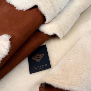 Op de afbeelding: Close-up van een bruin en wit schapenvachtkleed met een zwart label waarop "Impero London" staat.
