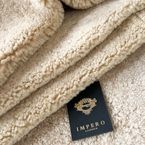May include: Close-up of a cream-coloured faux fur rug with a black tag that reads "Impero London".