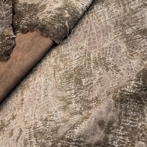 May include: A close-up of a brown and white patterned fabric with a textured surface. The fabric has a subtle sheen and a soft, fuzzy texture.