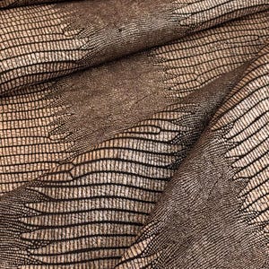 May include: A textured fabric featuring a repeating pattern of dark brown, elongated, scale-like shapes arranged in horizontal bands against a lighter, metallic bronze background, creating a layered, dimensional appearance across the surface.