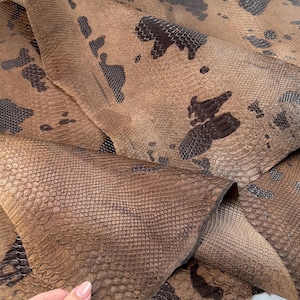 May include: A piece of brown snakeskin leather with a dark brown pattern. The leather is folded in half and has a soft, textured surface.