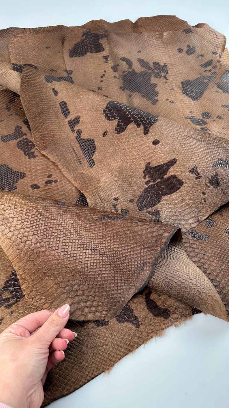 May include: A piece of brown snakeskin leather with a dark brown pattern. The leather is folded in half and has a soft, textured surface.