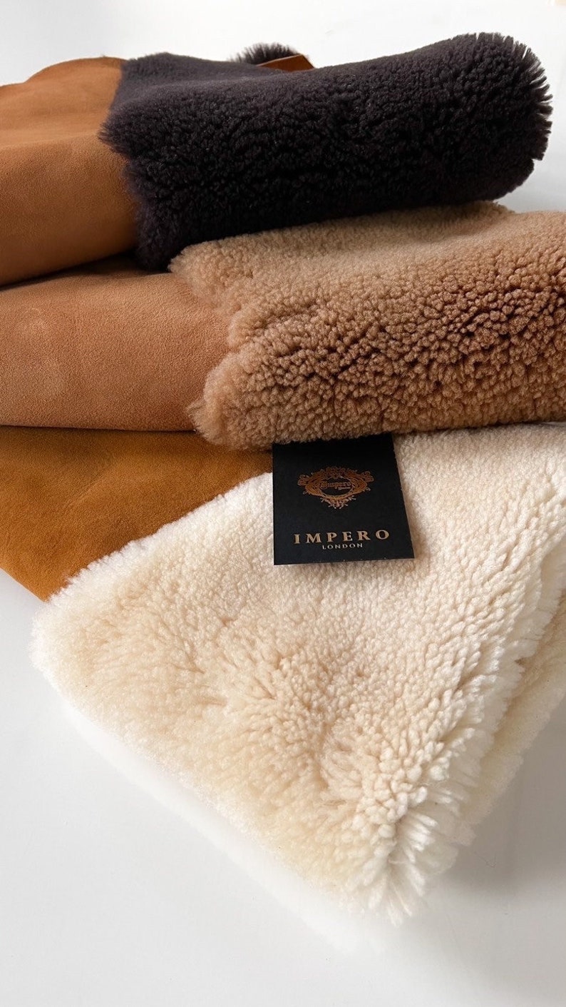 May include: Four pieces of sheepskin in different colors, including brown, tan, and white. The sheepskin is folded and stacked on top of each other. A black tag with gold lettering reads "Impero London".