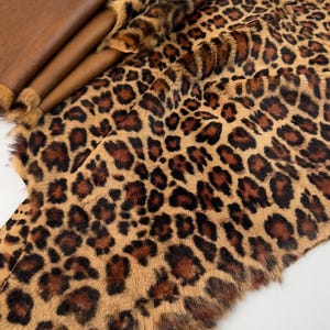 May include: A brown and black faux fur fabric with a leopard print pattern. The fabric has a soft, fluffy texture and is ideal for crafting projects.