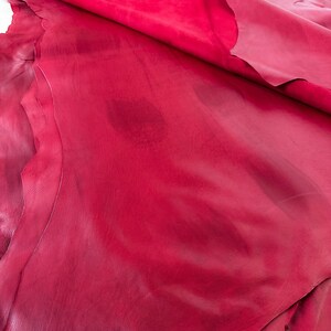 Pu&ograve; includere: Primo piano di un pezzo di pelle rossa piegato. La pelle ha una superficie liscia, leggermente strutturata e un colore rosso ricco e profondo.