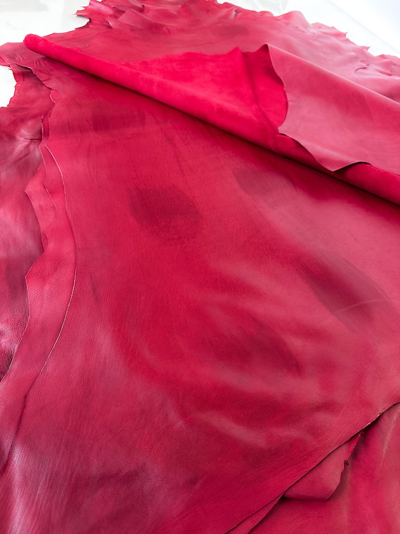Pu&ograve; includere: Primo piano di un pezzo di pelle rossa piegato. La pelle ha una superficie liscia, leggermente strutturata e un colore rosso ricco e profondo.