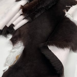 May include: A stack of brown sheepskin hides with a white underside. The hides are folded and have a soft, fluffy texture.