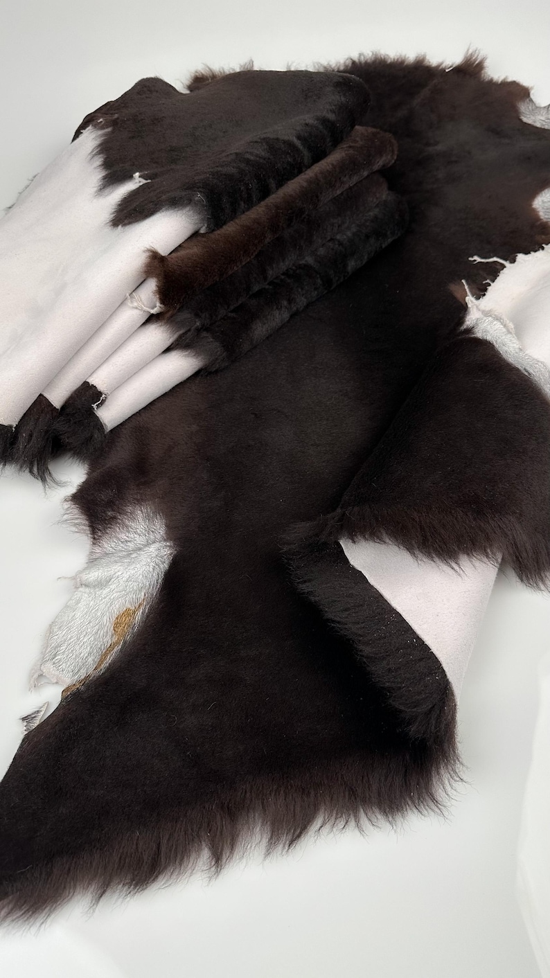 May include: A stack of brown sheepskin hides with a white underside. The hides are folded and have a soft, fluffy texture.