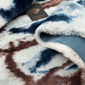 Könnte beinhalten: Nahaufnahme einer Kunstfell-Wurfdecke mit blauem, braunem und weißem Batikmuster. Die Decke hat eine weiche, plüschige Textur und eine blaue Wildleder-Rückseite. Ein schwarzes Etikett mit goldfarbenem Schriftzug lautet "IMPERO LONDON".