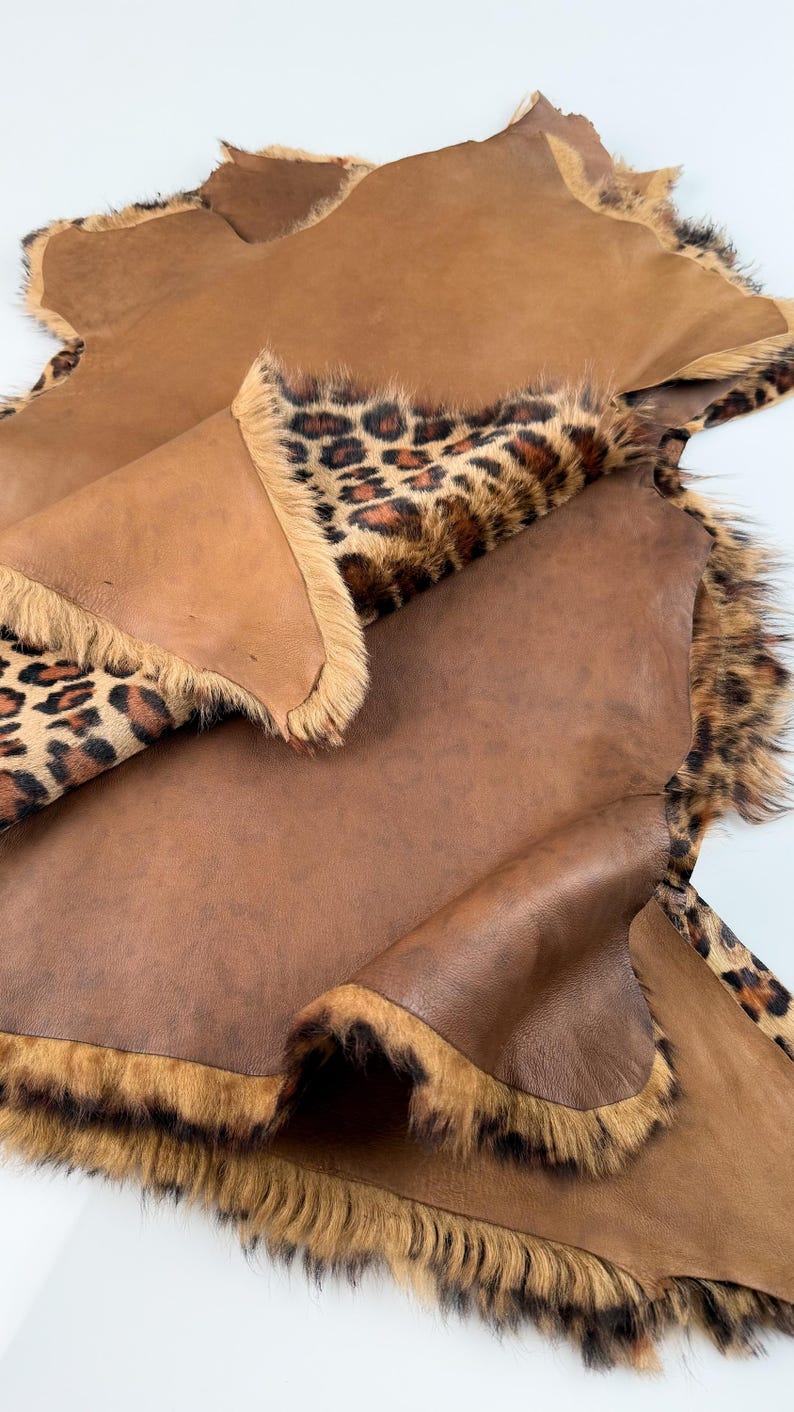 May include: A brown leather hide with a leopard print fur lining. The hide is folded in half and the fur is visible on the outside.