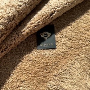 May include: Close-up of a brown faux fur throw blanket with a black label that reads "Impero London".