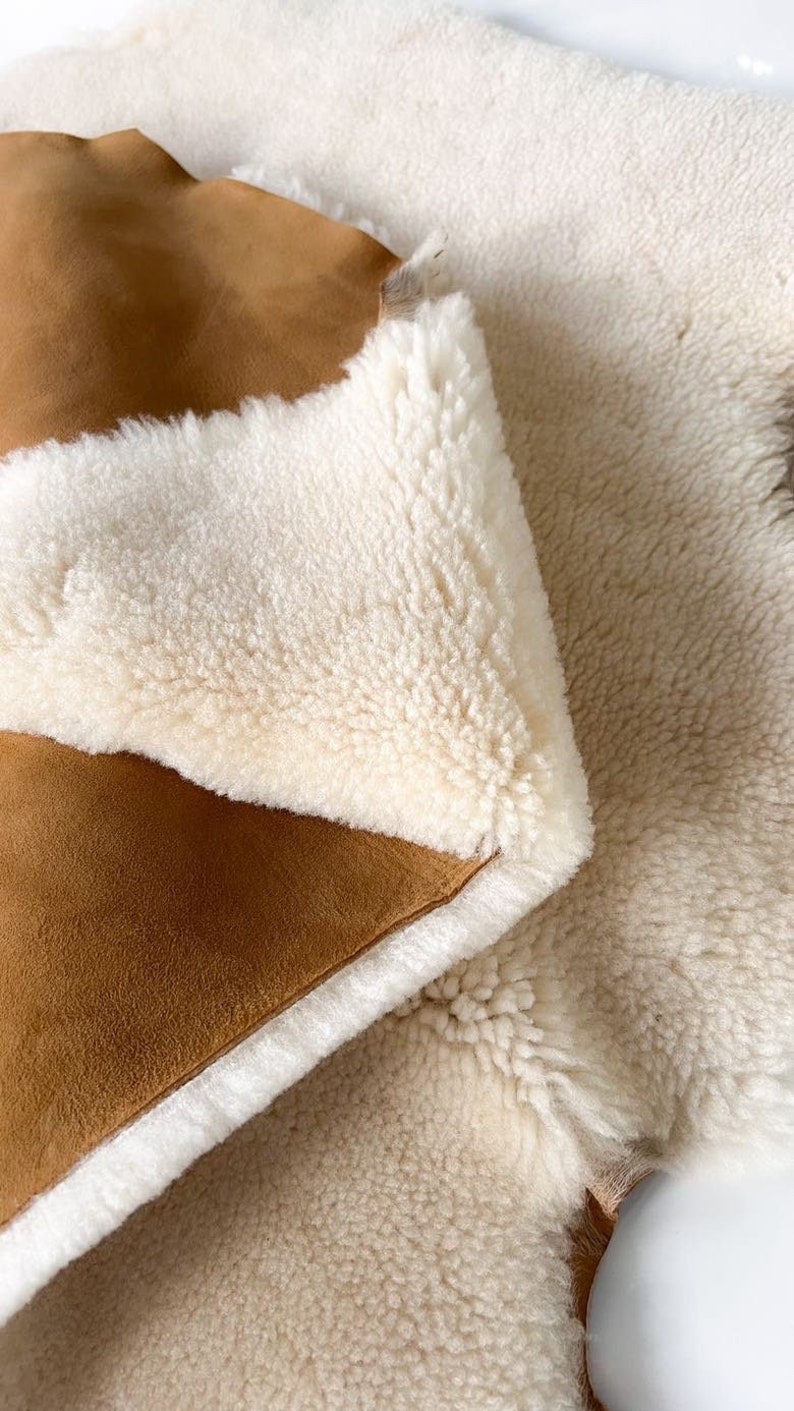 May include: A brown suede and white sheepskin rug with a soft, fluffy texture. The rug is folded in half, showing both sides of the material.