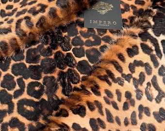 May include: A close-up shot of a leopard print hide. The hide displays a pattern of black spots on a tan and brown backdrop. A black tag with gold text reading "IMPERO LONDON" is visible.
