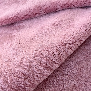 May include: Close-up of a soft, plush fabric in a dusty rose colour. The fabric has a fuzzy texture and is folded in half.