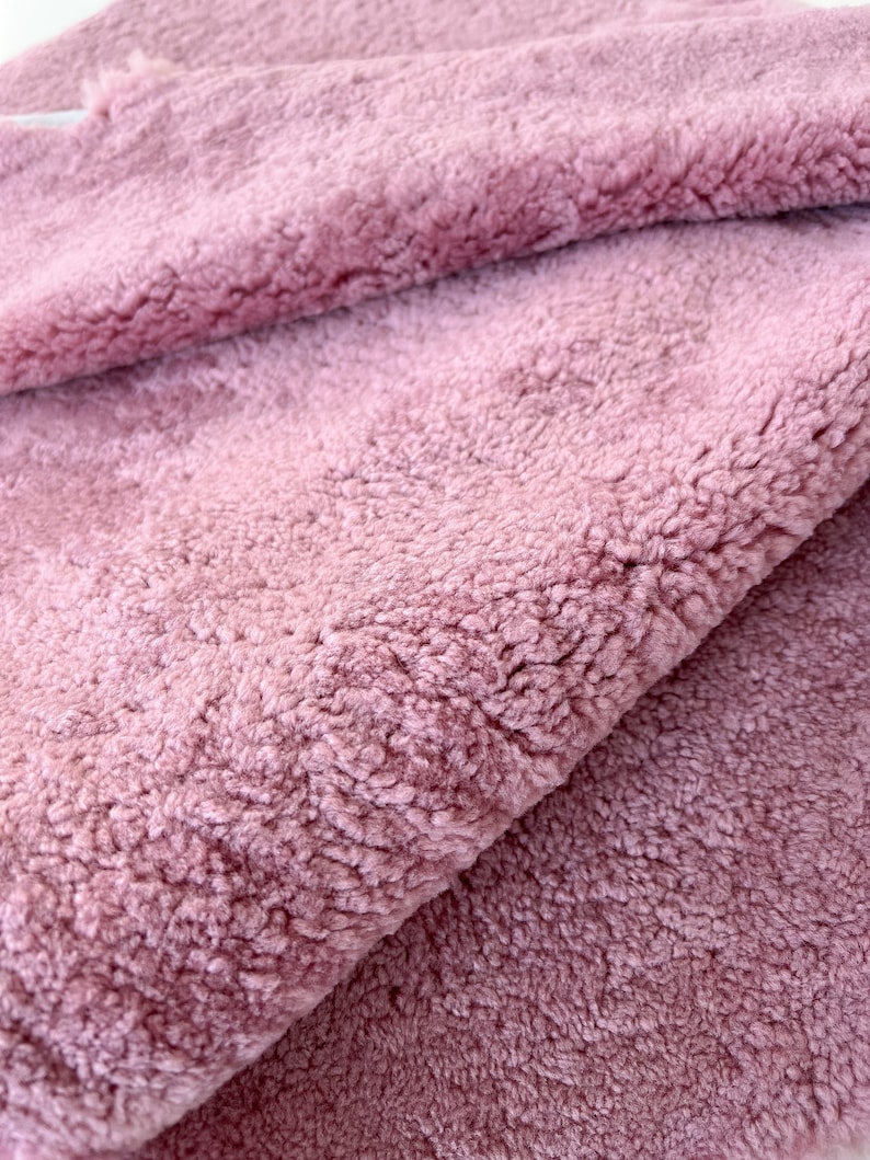 May include: Close-up of a soft, plush fabric in a dusty rose colour. The fabric has a fuzzy texture and is folded in half.