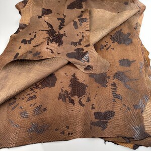 May include: A folded piece of brown snakeskin leather with a dark brown pattern. The leather has a textured surface and is folded in half.