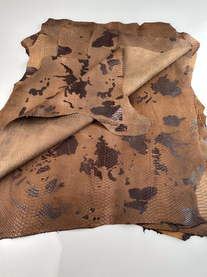 May include: A folded piece of brown snakeskin leather with a dark brown pattern. The leather has a textured surface and is folded in half.