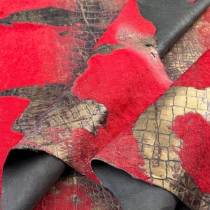 Könnte beinhalten: Roter und goldener Kunstpelzstoff mit Krokodilmuster. Der Stoff ist über sich selbst gefaltet und zeigt die verschiedenen Texturen.