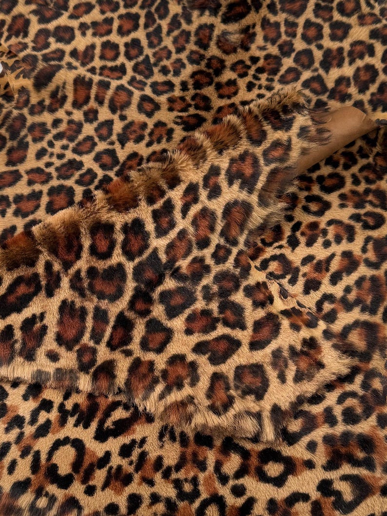 May include: Close-up of a brown and black leopard print faux fur fabric. The fabric has a soft, plush texture and is ideal for crafting projects.