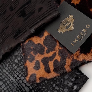 May include: Close-up of various animal print fabrics. The image features a black fabric with a textured pattern, a leopard print, and a black snakeskin print. A tag with the text "IMPERO LONDON" is visible.