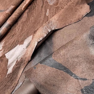 Puede incluir: Primer plano de una variedad de pieles de cuero marrón con diferentes texturas y patrones. Las pieles están dispuestas en capas y se superponen, mostrando la belleza natural del material.