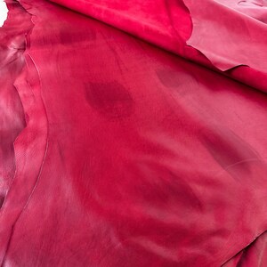 Pu&ograve; includere: Primo piano di un pezzo di pelle rossa piegato. La pelle ha una superficie liscia, leggermente strutturata e un colore rosso ricco e profondo.