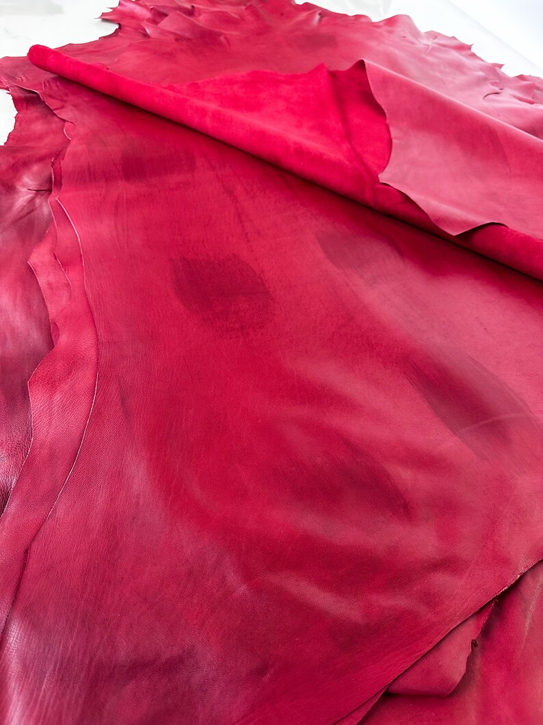Pu&ograve; includere: Primo piano di un pezzo di pelle rossa piegato. La pelle ha una superficie liscia, leggermente strutturata e un colore rosso ricco e profondo.