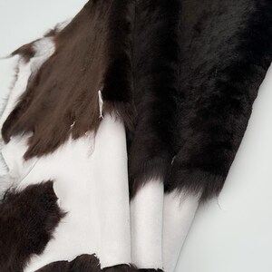 May include: A brown and white sheepskin rug with a soft, fluffy texture. The rug is folded in half, revealing the white underside.
